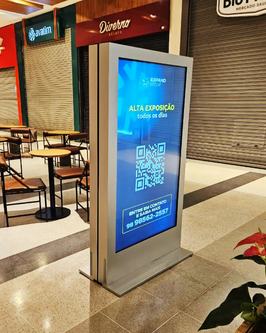 Totem digital Expand Mídia ao lado de prateleiras em um minimercado